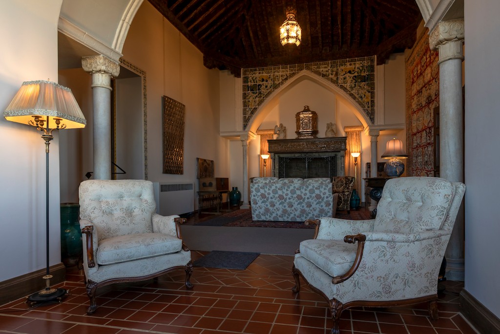 Cozy, vintage living room with patterned armchairs, tile floor, and a decorated fireplace centerpiece under a dark wooden ceiling