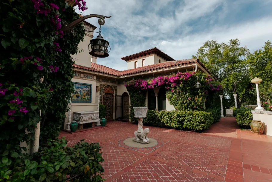Mediterranean-style courtyard with red-tiled roof, flowering bougainvillea, and a stone lion fountain on a brick-paved patio.