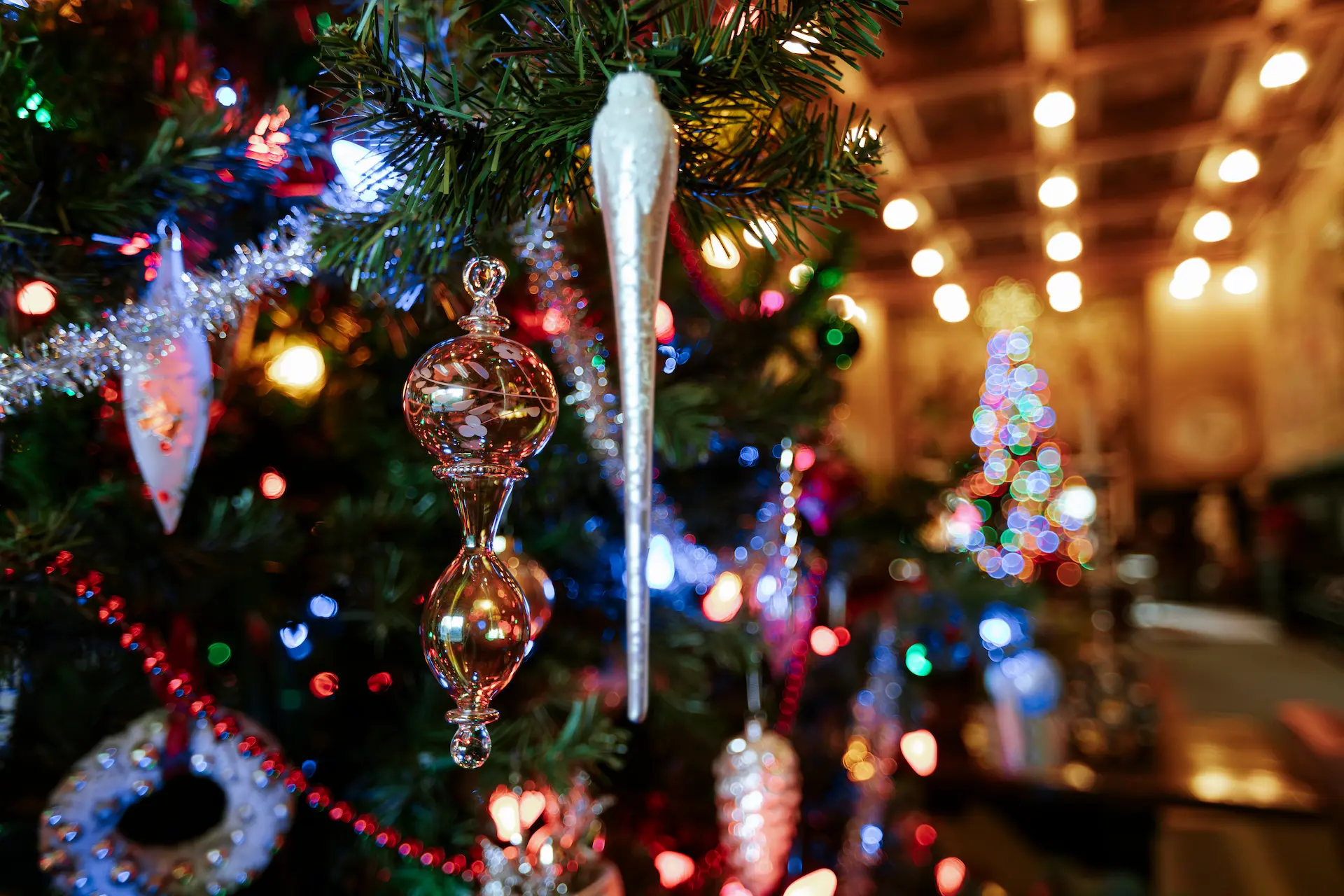 Close-up of a glass Christmas ornament on a tree with colorful bokeh lights in the background.